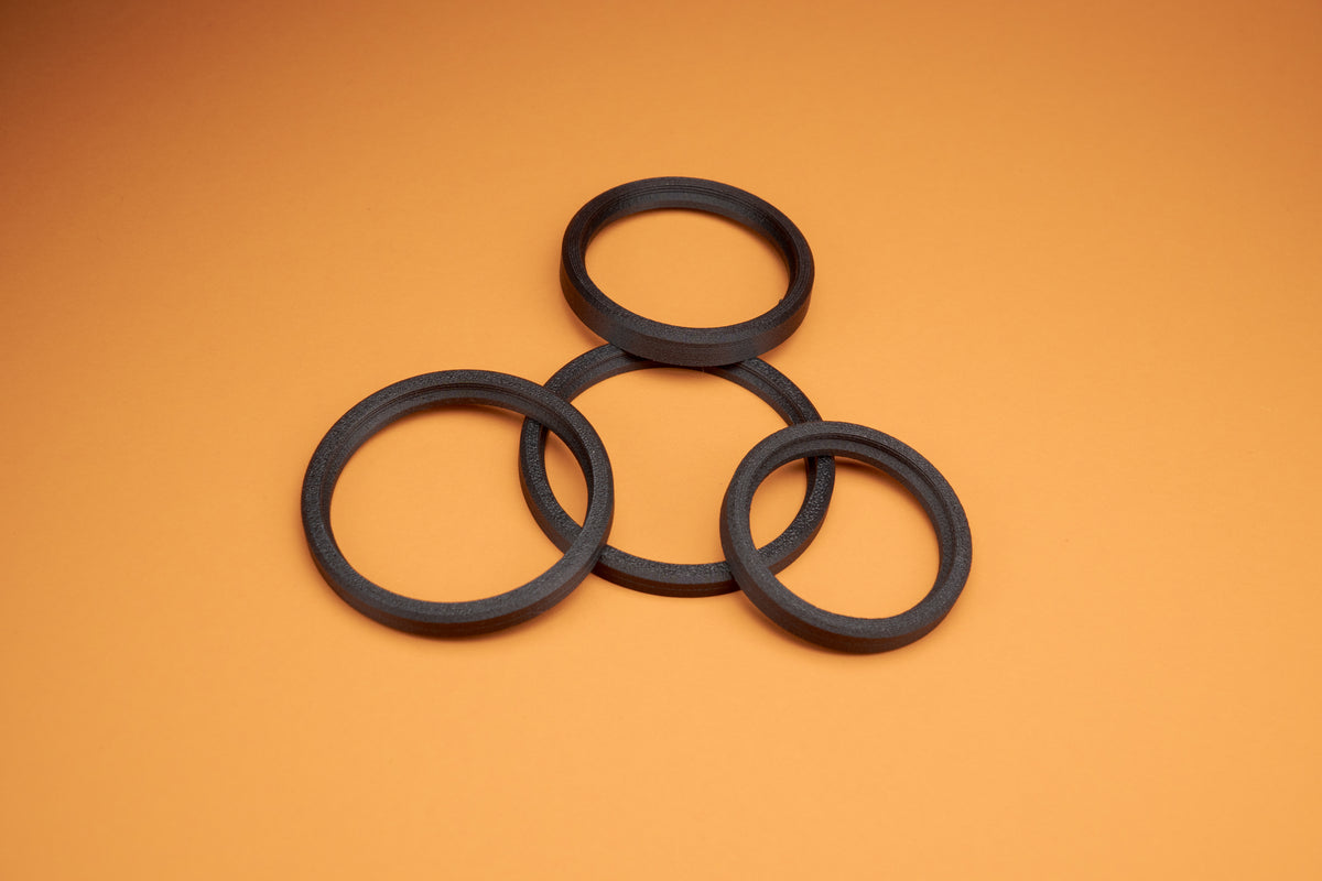Five black Akara Labs Stealth rings laying on orange background