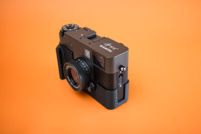 Fujifilm X half in Akara Labs Slim Skin Case with grip, front three-quarter view, orange background