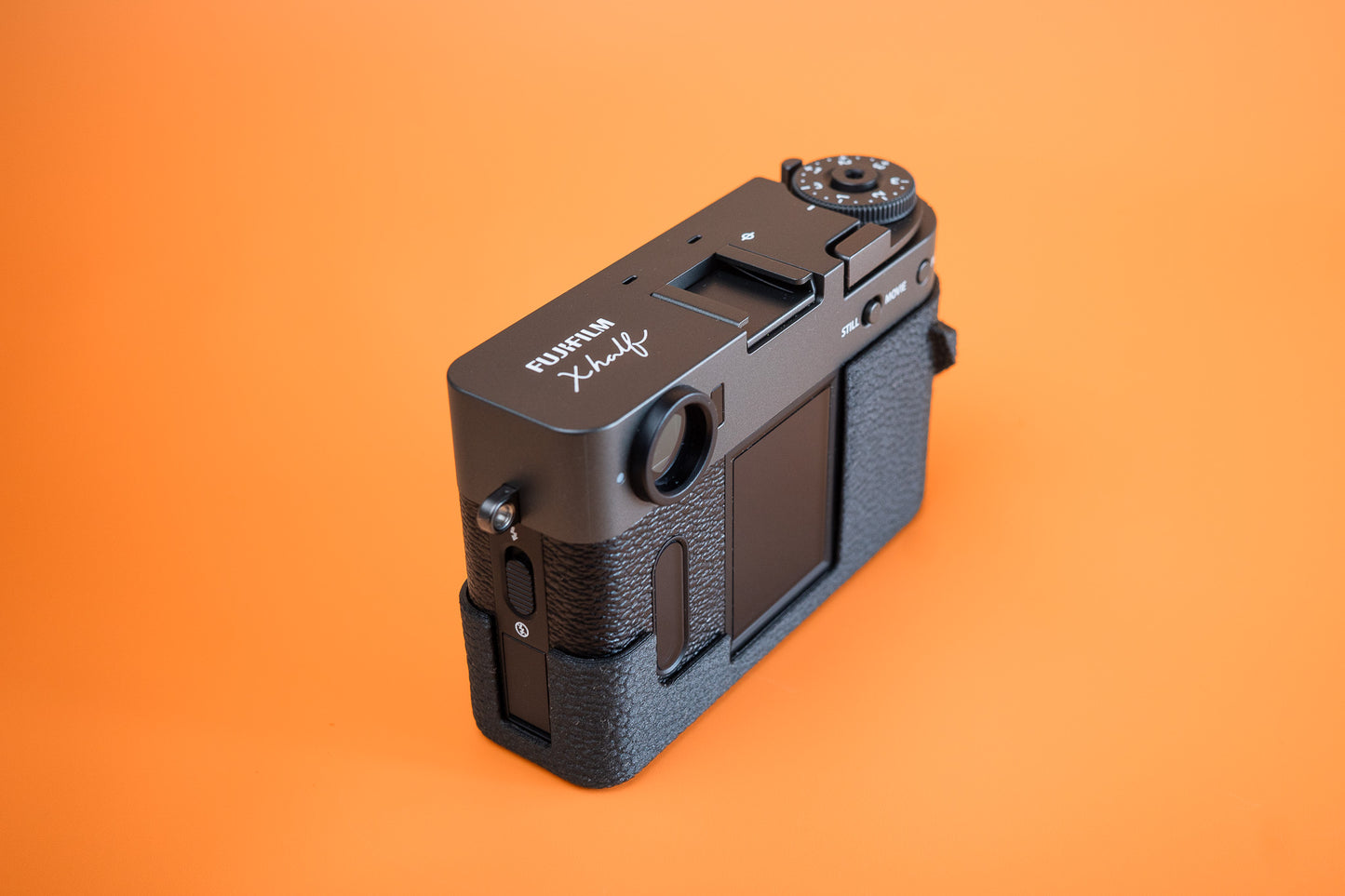 Fujifilm X half in Slim Skin Grip Case with thumb grip, left side profile showing leatherette-textured TPU