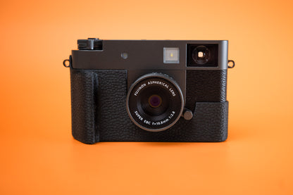 Fujifilm X half in Slim Skin Case with grip, front view on orange background