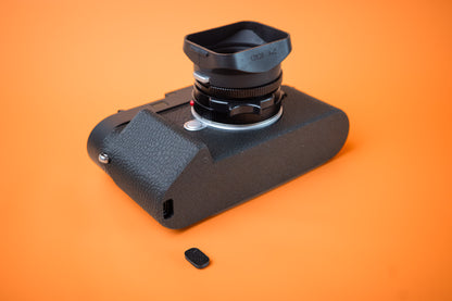 Akara Labs Leica M11 Slim Skin Grip case. Bottom view showing USB-C port access. Orange background.