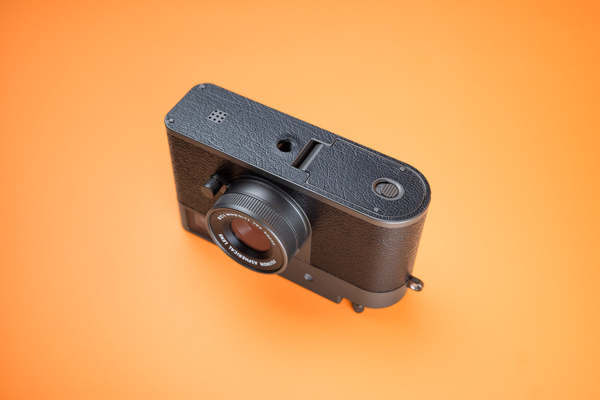 Akara Labs black vinyl base protector or fuji x half camera. front underside view on orange background.