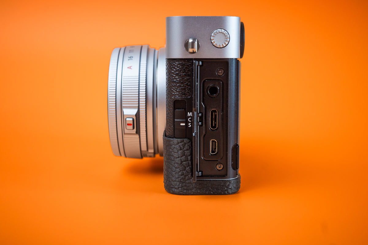Fujifilm X-E5 in silver, left side view of connection ports, fitted with an Akara Labs Slim Skin grip case in black leatherette-textured TPU