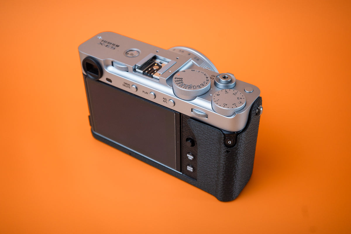 Fujifilm X-E5 in silver, rear right view, fitted with an Akara Labs Slim Skin no-grip case in black leatherette-textured TPU