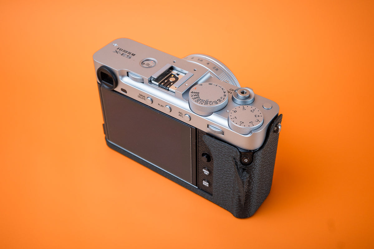 Fujifilm X-E5 in silver, rear right view, fitted with an Akara Labs Slim Skin Grip case in black leatherette-textured TPU