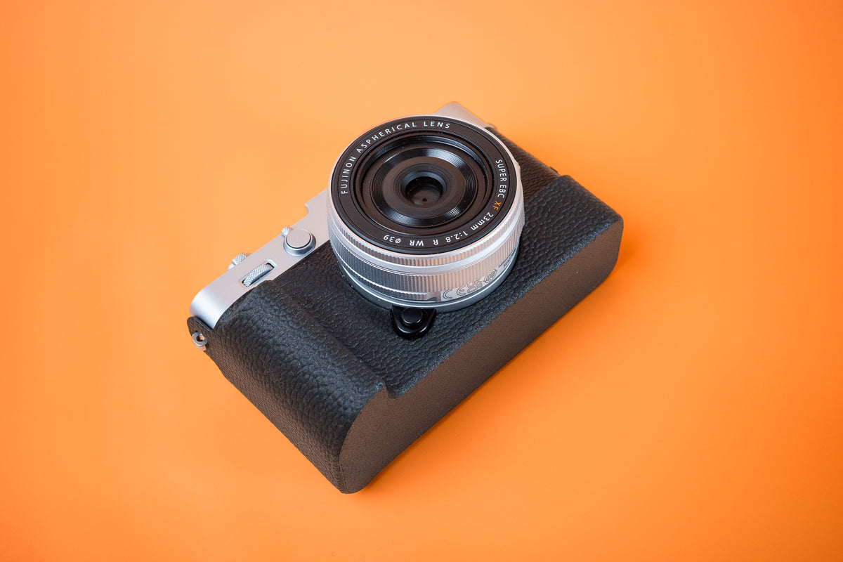 Fujifilm X-E5 in silver, front bottom view, fitted with an Akara Labs Slim Skin grip case in black leatherette-textured TPU