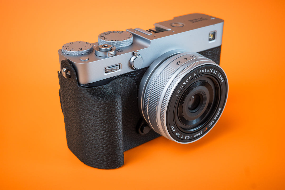 Fujifilm X-E5 in silver, front right view, fitted with an Akara Labs Slim Skin grip case in black leatherette-textured TPU
