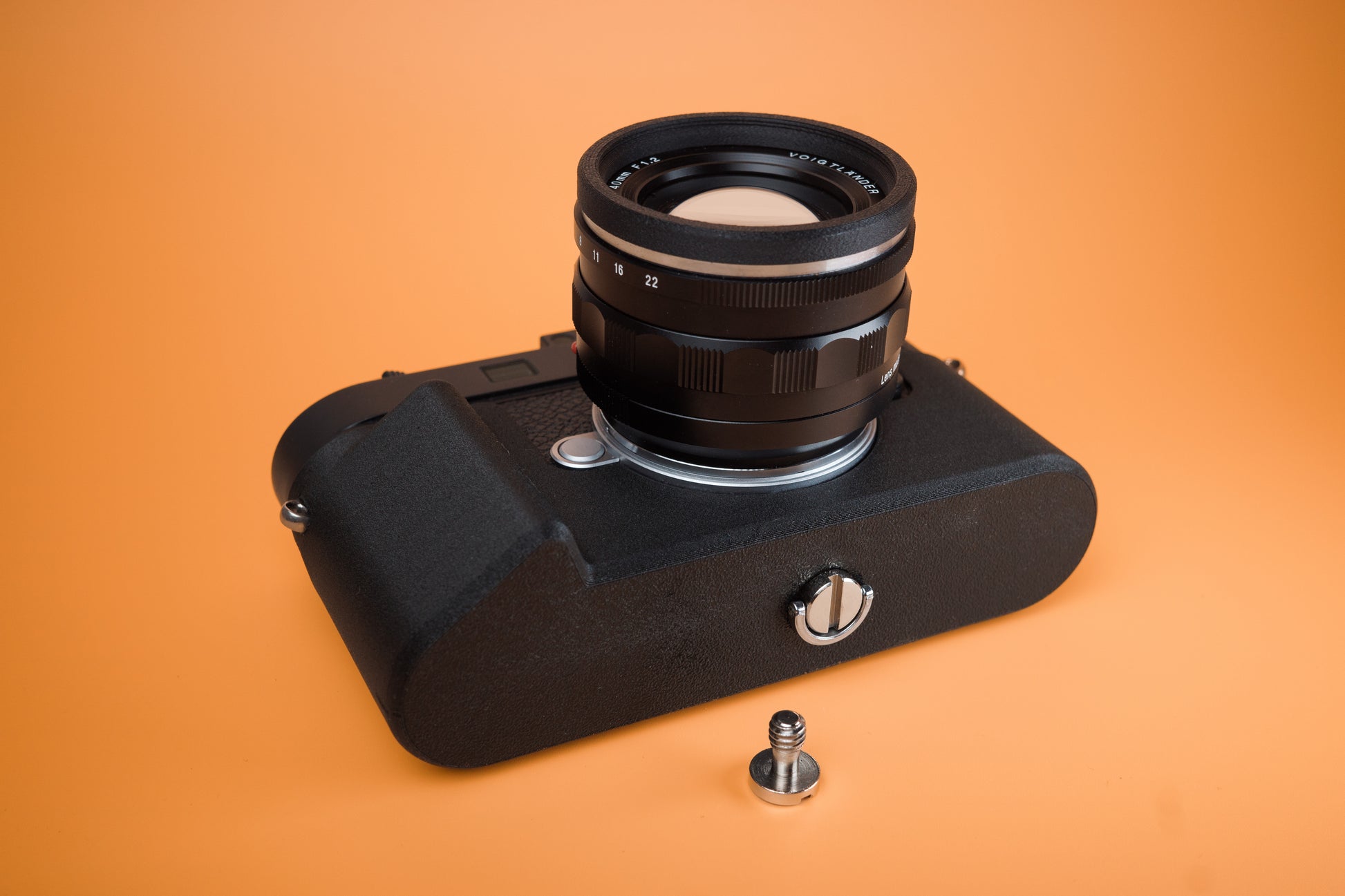Leica M11 Slim Skin Tripod version case with two mounting screws. Bottom view with camera laying on rear. Orange background.