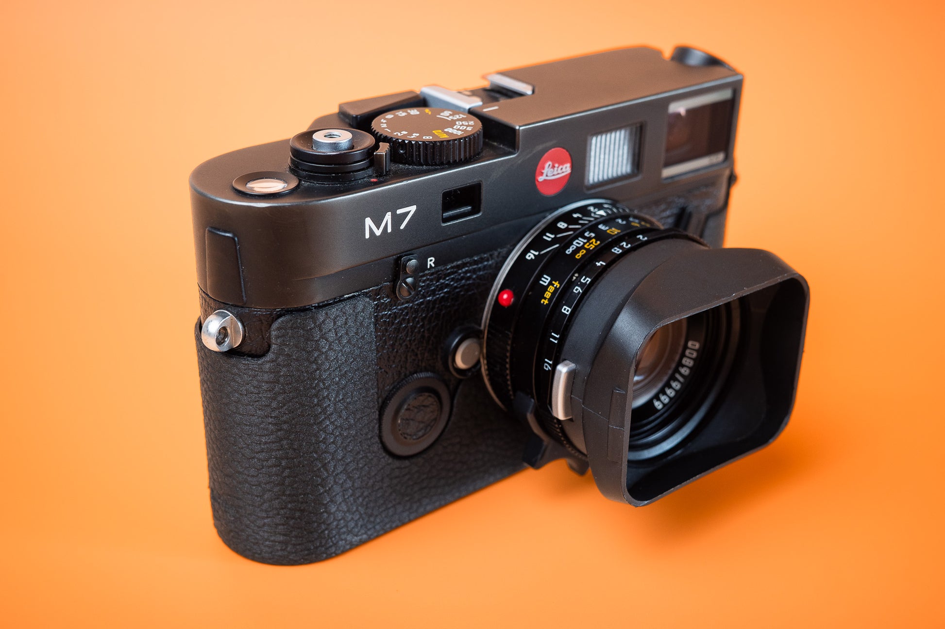 Leica M7 black leatherette-textured style Slim Skin standard case. Front right view, photographed against an orange background.